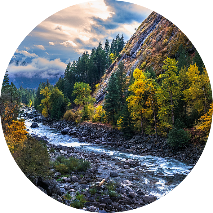 flowing river with mountain, trees, and clouds in the background